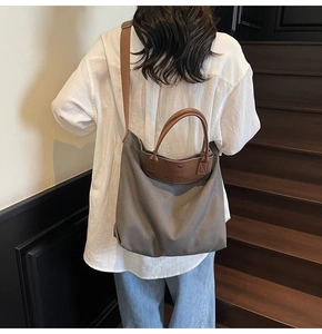 Detail view of the gray canvas tote bag with brown leather handles worn by a model