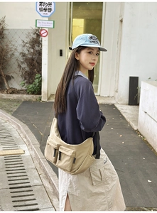 Detail of beige nylon crossbody bag featuring front flap pockets and tactical webbing straps