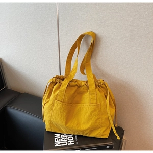 Detail of a casual yellow nylon drawstring tote bag with a front pocket on dark surface