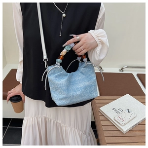 Detail of light blue denim bucket bag with colorful pearl handle and white strap