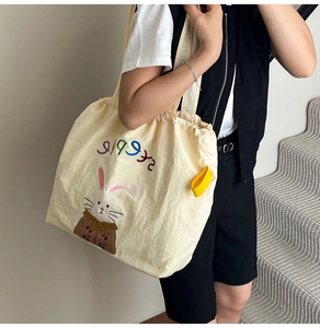 Close-up of beige canvas tote bag with bunny patch and colorful letter embroidery details