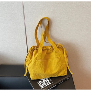 Detail of a ginger yellow drawstring nylon tote bag with front pocket on a black surface