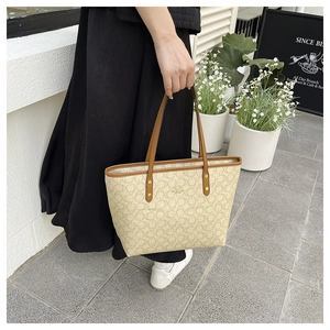 Close-up of beige monogram tote bag with brown leather handles and gold metal rings