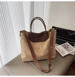Detail view of large canvas tote bag with brown fabric strap and leather patch logo
