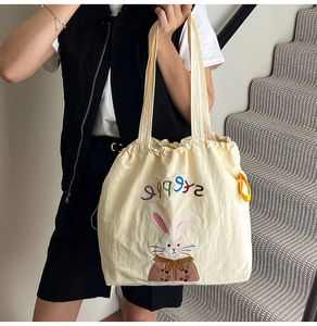 Detail of cute rabbit embroidery and rainbow text on beige canvas drawstring tote bag