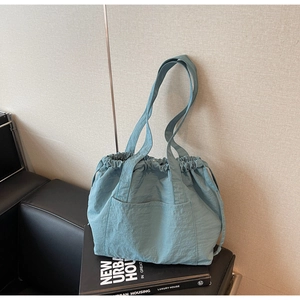 Detail of grey-blue nylon tote bag with drawstring closure on a beige background