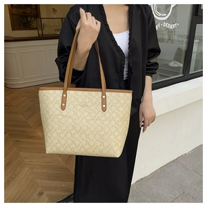 Chic beige tote bag with chain print and brown leather handles shown in a cafe setting