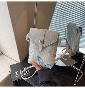 Détail du sac à bandoulière bleu brodé avec boucle magnétique dorée en forme de coeur