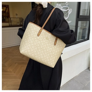 Close-up of beige tote bag with monogram texture and brown leather handles in city setting