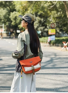 Outdoor lifestyle shot of a vibrant orange nylon crossbody bag with side woven detail
