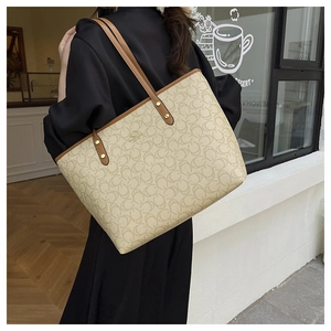 Detail of beige monogram tote bag with brown leather handles and gold rivet accents