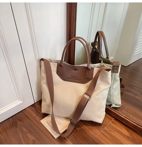 Detail of canvas tote bag showing brown leather handles and adjustable shoulder strap