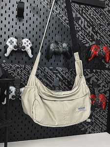 Large beige nylon hobo crossbody bag with wide strap on industrial pegboard background