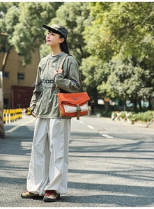 Outdoor view of orange and beige nylon messenger bag with buckle worn by casual model