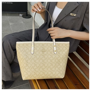 Detail of classic beige tote bag with monogram pattern and gold logo on a wooden bench
