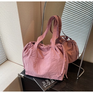 Detailed view of light pink nylon tote bag with drawstring sides and large front pocket