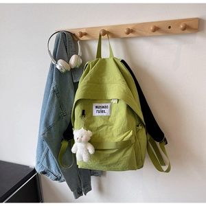 Dettaglio dello zaino in nylon verde lime con ciondolo a forma di orsetto e logo in tessuto