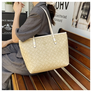 Detail of monogram tote bag with gold hardware and slim straps in outdoor cafe setting
