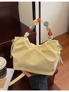 Pleated light yellow bucket bag with colorful beaded handle and leather strap