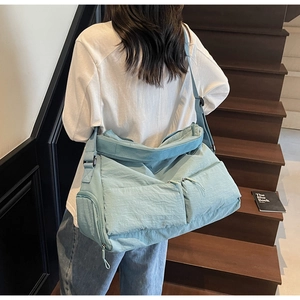 Detail of light blue nylon tote bag showing multiple zipper pockets and wide strap