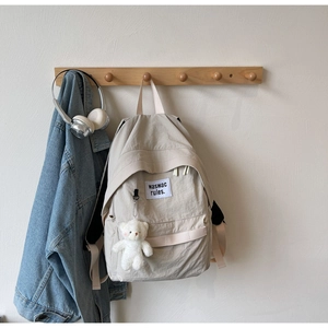 Zaino in nylon beige con ciondolo a orsetto appeso a un gancio di legno a muro