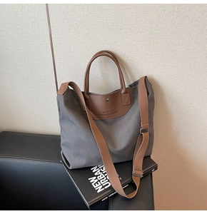 Close-up of gray canvas tote bag with brown leather handles on decorative books
