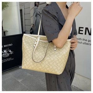 Detail of a beige tote bag with logo pattern, zipper closure and golden hardware