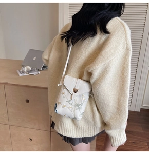 Détail de broderie florale sur sac de téléphone en cuir blanc avec boucle cœur dorée