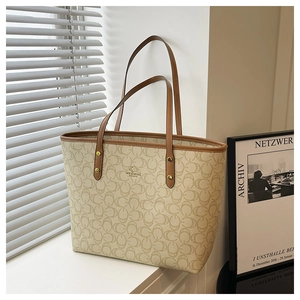 Close-up of beige tote bag with monogram pattern, brown leather trim and gold logo