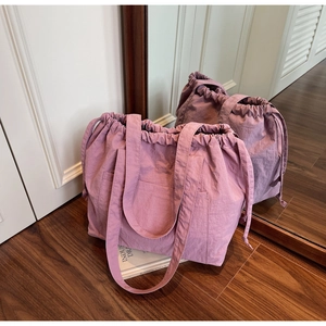 Detail of mauve nylon tote bag with drawstring closure and large front pocket on wood floor