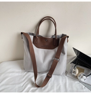 Minimalist canvas tote bag with brown leather trim and shoulder strap in workspace setting