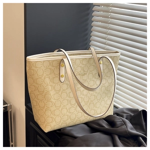 Macro detail of beige monogram tote bag featuring metal logo and premium gold hardware studs