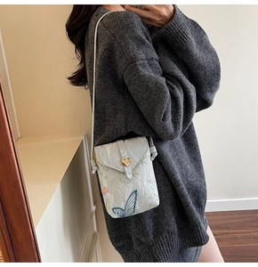 Détail du sac de téléphone blanc avec broderie papillon bleue et fermoir cœur doré