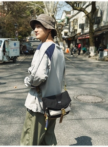 Detail of a black and beige nylon messenger bag with adjustable brown strap in a street setting