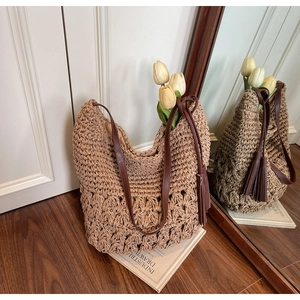 Detail of woven straw tote bag featuring brown leather straps and long tassel charm