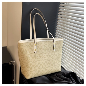 Detail of beige tote bag featuring C-pattern texture, slim straps and gold stud accents