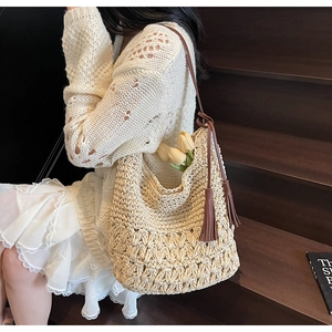 Detail of woven straw shoulder bag featuring brown leather strap and tassel ornament