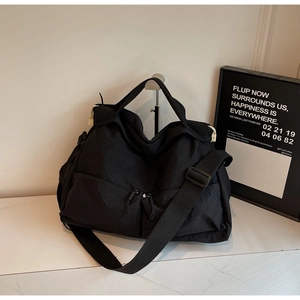 Detail of black nylon tote bag featuring front dual zipper pockets and adjustable wide strap