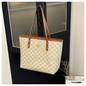 Detail of elegant cream tote bag with logo pattern, brown leather handles and gold metal tag