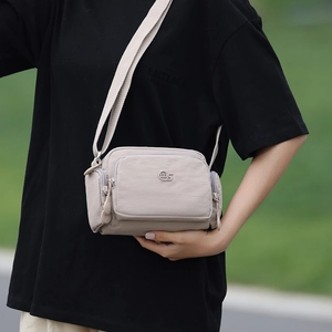 Dettaglio borsa a tracolla in nylon beige con tre tasche con zip e tracolla in tessuto