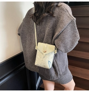 Détail du sac bandoulière brodé vert clair avec une boucle en métal doré en forme de cœur