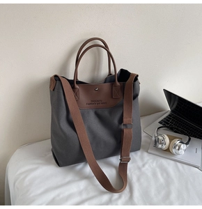 Detail of grey canvas tote bag featuring brown leather trim and stylish branding