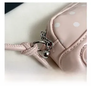 Detail of pink polka dot handbag showing silver zipper hardware and knotted shoulder strap