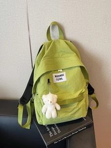 Zaino minimalista in nylon verde con portachiavi a orsetto e logo su un divano