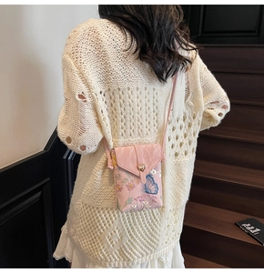 Détail du sac de téléphone rose brodé avec boucle en cœur doré sur une robe blanche