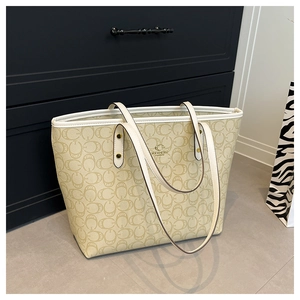 Close-up of beige monogram tote bag with brown pattern and polished metal logo detail