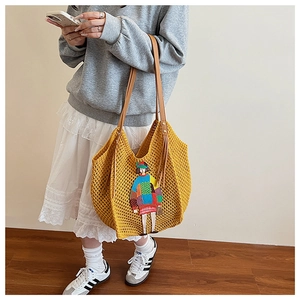 Detail of yellow knit tote bag featuring cartoon embroidery and brown leather handles