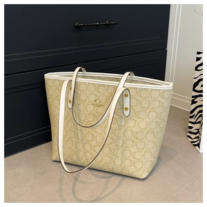 Detailed close-up of beige tote bag with logo pattern and gold metallic rivet hardware