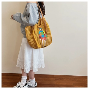 Detail of yellow knit tote bag featuring colorful cartoon embroidery and leather strap