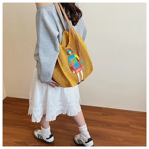 Detail of yellow knit tote bag featuring colorful cartoon embroidery and leather straps